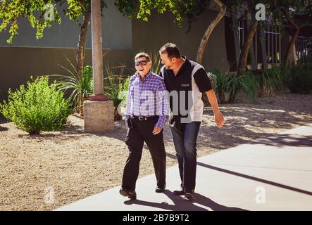 Deux hommes caucasiens d'âge moyen rient tout en convergeant et marchant sur une journée ensoleillée sur un sentier dans le canal de l'Arizona à Scottsdale, AZ, États-Unis Banque D'Images