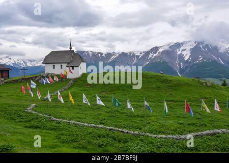 Une église avec beaucoup de drapeaux dans le village suisse Bettmeralp un jour nuageux Banque D'Images