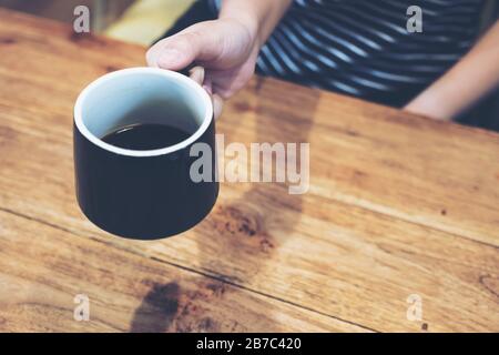 Gros plan de la main de la femme tenant un café noir sur une table en bois vintage Banque D'Images