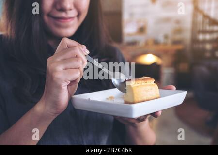 Gros plan image d'une heureuse femme tenant et apprécier manger gâteau au fromage avec cuillère dans le café Banque D'Images
