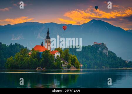 Superbe paysage alpin avec des montgolfières colorés au-dessus du château et du lac Bled au lever du soleil, Bled, Slovénie, Europe Banque D'Images