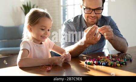 Papa souriant et petite fille mignonne faisant des bracelets. Banque D'Images