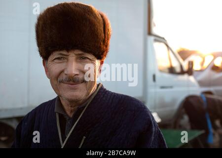 Portrait d'un homme portant un manteau traditionnel et un chapeau de fourrure sur le marché du bétail du matin dans un village près de Boukhara, Ouzbékistan Banque D'Images