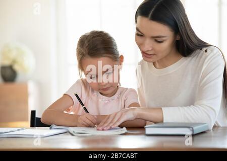 Affectueuse jeune mère enseignant la petite fille lecture écriture. Banque D'Images