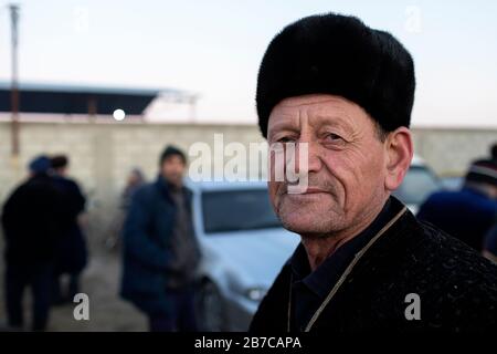 Portrait d'un homme portant un manteau traditionnel et un chapeau de fourrure sur le marché du bétail du matin dans un village près de Boukhara, Ouzbékistan Banque D'Images