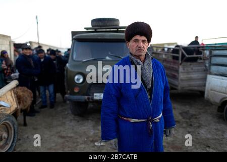 Portrait d'un homme portant un manteau traditionnel et un chapeau de fourrure sur le marché du bétail du matin dans un village près de Boukhara, Ouzbékistan Banque D'Images
