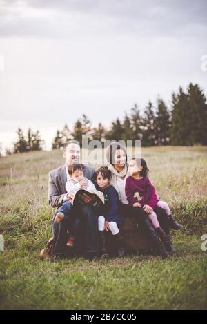 Belle famille joyeuse avec une mère, un père et trois enfants lisant la Bible dans le parc Banque D'Images