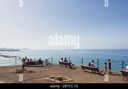 Les vacanciers de Tenerife, aux îles Canaries, en Espagne, profitent d'une autre journée ensoleillée sur des bancs face à l'océan Atlantique à Costa Adeje Banque D'Images