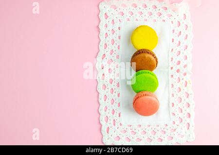 Plusieurs macarons multicolores aux couleurs pastel sur une serviette blanche sur fond rose Banque D'Images