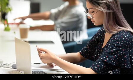 Femme d'affaires asiatique portant des lunettes à l'aide d'un téléphone, lisant un e-mail professionnel Banque D'Images
