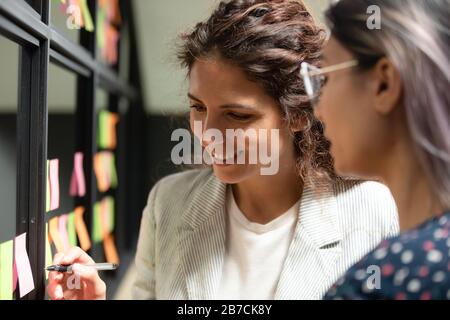 Femme d'affaires souriante écrivant des notes sur des papiers collants sur le mur de verre Banque D'Images