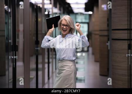 Une femme d'affaires heureuse d'âge moyen célèbre le succès au bureau Banque D'Images