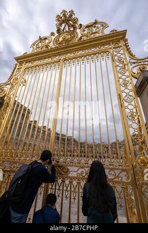 Tourisme prenant des photos à travers les bars dorés de la porte du Château de Versailles dans la périphérie de Paris, France, Europe Banque D'Images