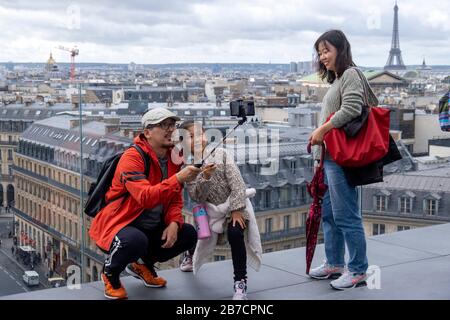 La famille asiatique prend des photos avec un bâton de selfie du toit des Galeries Lafayette avec la Tour Eiffel en arrière-plan, Paris, France Banque D'Images