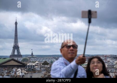 Un couple asiatique prend des photos avec un bâton de selfie du toit des Galeries Lafayette avec la Tour Eiffel en arrière-plan, Paris, France Banque D'Images