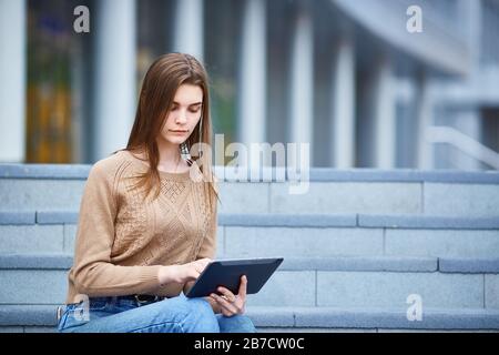 Une jeune fille est assise sur les marches et regarde la tablette Banque D'Images