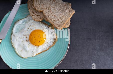 Oeuf biologique frit côté ensoleillé assaisonné avec sel et poivre sur une plaque avec pain de grain entier sur le côté. Vue de dessus. Banque D'Images