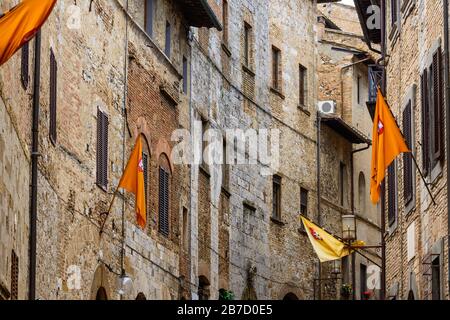 Une rue en courbe avec de nombreuses fenêtres et drapeaux orange volantes sur les murs dans le centre historique de San Gimignano, province de Sienne, Toscane, Italie. Banque D'Images