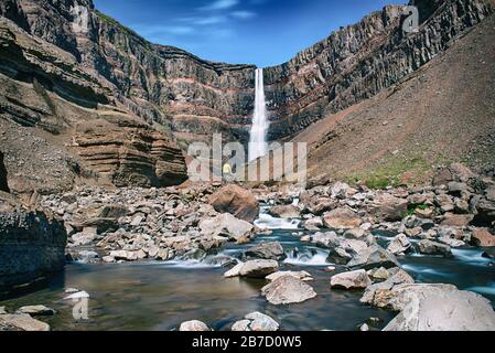 Homme debout près de la Hengifoss Cascade dans l'Est de l'Islande avec river au premier plan sur le paysage voyage naturel. Banque D'Images