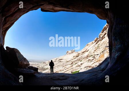 Silhouette d'homme debout devant une entrée de grotte dans la montagne du désert de l'est du Kazakhstan Banque D'Images