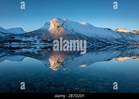 Une belle photo d'une montagne enneigée au coucher du soleil, reflet dans les eaux calmes d'un fjord. Cette image a été prise près de Tromso en Norvège. Banque D'Images