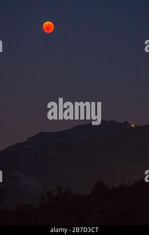 La lune rouge et Mars se levant derrière les montagnes la nuit avec un ciel plein d'étoiles Banque D'Images