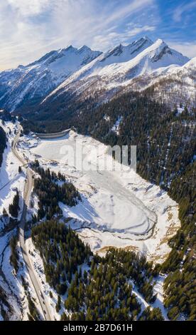 Vue aérienne sur le lac et le barrage glacé du Lago d'Isola, et sur la route du col San Bernardino. Graubünden, district de Moesa, Suisse, Europe. Banque D'Images