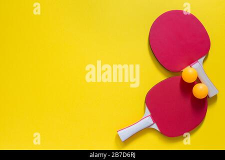 Raquettes de ping-pong de tennis rouge et boules d'orange isolées sur fond jaune, équipement de sport pour le tennis de table Banque D'Images