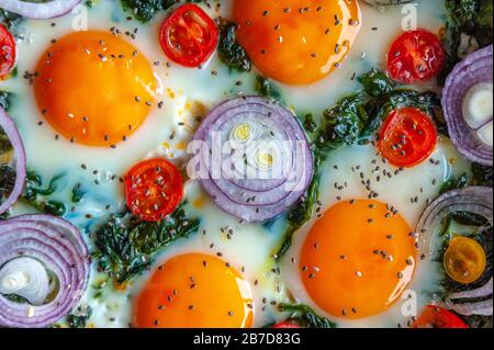 Détail d'une omelette aux épinards dans une poêle et décorée avec de l'oignon frais, des tomates et des épinards Banque D'Images