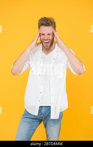 Migraine de tête et spasme. Problèmes de santé. Vie d'affaires. Mal de tête horrible. Bel homme dans un Jean chemise souffrant de douleur de tête. Homme fatigué et stressant fond jaune. Concept de vie stressante. Banque D'Images