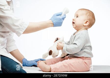 Le pédiatre ou l'infirmière vérifie la température corporelle du bébé garçon à l'aide d'un thermomètre frontal infrarouge (pistolet thermomètre) pour les symptômes de maladie Banque D'Images