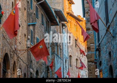 Drapeaux rouges volantes sur les murs de la rue via S. Matteo dans le centre historique de San Gimignano, province de Sienne, Toscane, Italie, au coucher du soleil. Banque D'Images