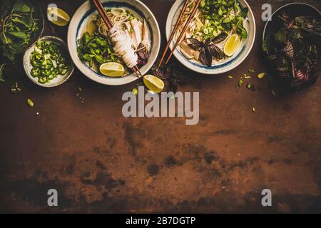 Déjeuner de cuisine asiatique. Plat de soupe de poulet à nouilles de riz vietnamienne Pho Ga avec cilantro frais, germes de soja, verts, chaux dans des bols avec des baguettes Banque D'Images