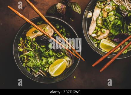 Déjeuner de cuisine asiatique. Plat de soupe de poulet à nouilles de riz vietnamienne Pho Ga avec cilantro, germes de soja, verts, chaux dans des bols avec baguettes en bois o Banque D'Images