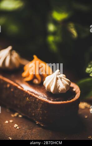 Dessert contemporain. Chocolat belge, merenge suisse et tarte au caramel sur fond sombre rouillé, gros plan, foyer sélectif. Café ou pâtisserie moderne Banque D'Images