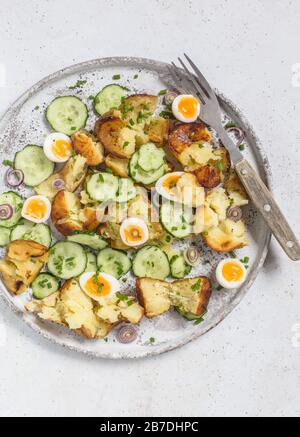 Salade de pommes de terre rôties, concombre et œufs de caille, servie sur une plaque grise. Banque D'Images