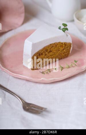 Tranche de gâteau aux carottes végétaliennes avec glaçage à la crème de noix de coco servi sur une plaque rose Banque D'Images