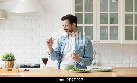 Drôle jeune homme chantant au fouet, cuisine dans la cuisine moderne Banque D'Images