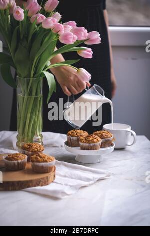 Muffins aux pommes de carotte sur un présentoir à gâteaux blanc et une femme qui verse du lait dans une tasse Banque D'Images