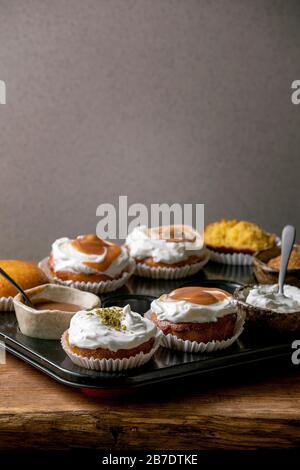 Oranges d'agrumes ou clémentines maison muffins doux cupcakes dans un plateau cuit avec différentes crèmes, pistaches, garnitures de caramel dans des bols au-dessus de bois Banque D'Images