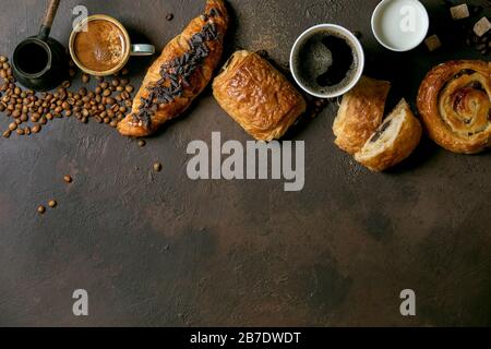 Variété de pains à base de raisins secs et de chocolat, croissant avec différentes tasses de café et de lait, cizve, cuillère en bois recyclé Banque D'Images