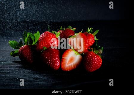 Belles fraises rouges avec fond noir et pluie légère Banque D'Images