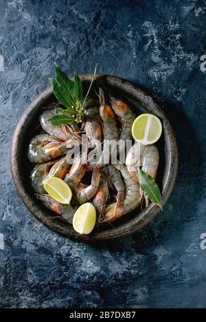 Crevettes non cuites à la crevette avec de la chaux et des herbes en plaque d'argile. Fond en béton foncé. Couche plate, espace de copie Banque D'Images