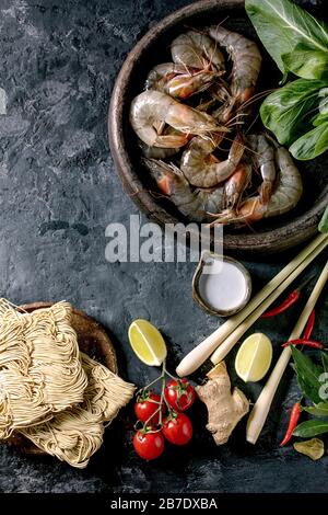 Crevettes à la crevette crue aux nouilles asiatiques, au lait de noix de coco et aux légumes. Ingrédients pour la cuisine du dîner asiatique ou soupe thaïlandaise tom yum. Fond en béton foncé. Banque D'Images