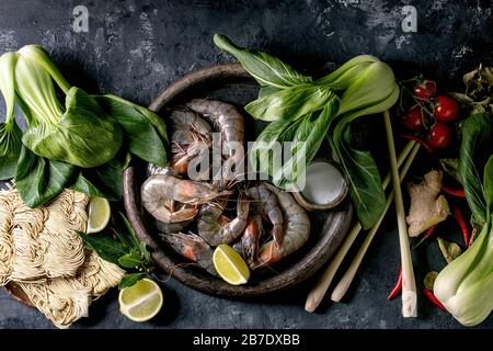 Crevettes à la crevette crue aux nouilles asiatiques, au lait de noix de coco et aux légumes. Ingrédients pour la cuisine du dîner asiatique ou soupe thaïlandaise tom yum. Fond en béton foncé. Banque D'Images