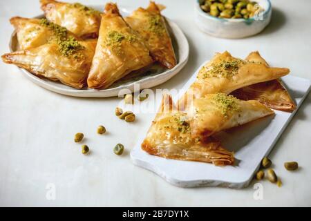 Baklava de dessert traditionnel turc maison avec pistache servie sur planche à découper en bois blanc avec bol de noix sur table en marbre blanc Banque D'Images