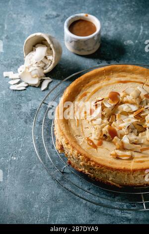 Cheesecake maison de sucre de canne à la noix de coco cuit sur un plateau de refroidissement avec garniture de caramel dans un bol en céramique sur fond de texture bleue. Banque D'Images