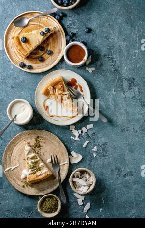 Morceaux de cheesecake avec différents garnitures sur plaques en céramique et variété de sauces dans des bols en céramique sur fond de texture bleue. Plat, espace Banque D'Images