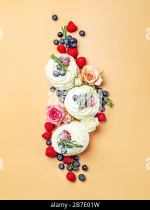 Superbe aménagement créatif de mini gâteaux pavlova dans la vue de dessus. Mini pavlova avec fleurs et baies sur fond jaune crème. Vertical Banque D'Images