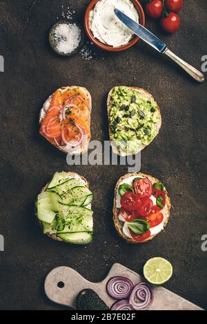 Variété de sandwichs et d'ingrédients. Purée d'avocat, mozzarella, tomates, basilic, fromage à la crème, saumon fumé, oignon rouge, pain de concombre à grains entiers Banque D'Images